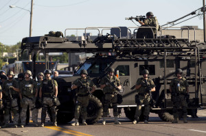 Law enforcement officers, including a sniper perched atop an armored vehicle, watch as demonstrators protest the fatal shooting of Michael Brown, in Ferguson, Mo.