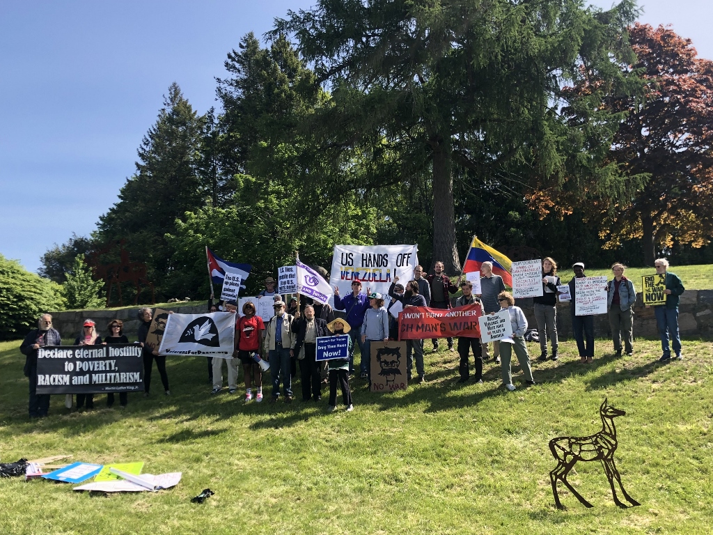 Peace activists holding signs and flags gather outside U.S. Coast Guard Academy to protest John Bolton