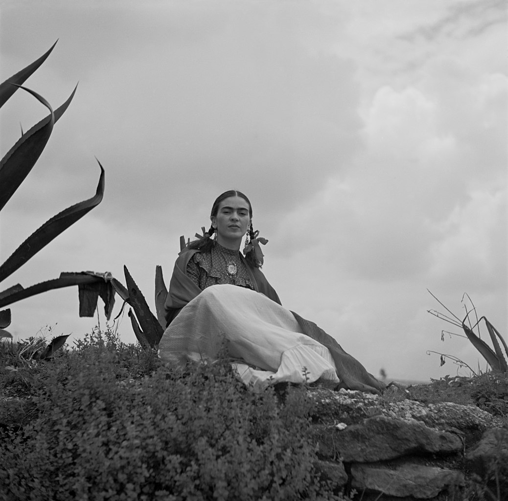 Frida Kahlo, seated next to an agave plant, from a 1937 photo shoot for Vogue entitled "Señoras of Mexico." Photo by Toni Frissell, from Wikimedia Commons.