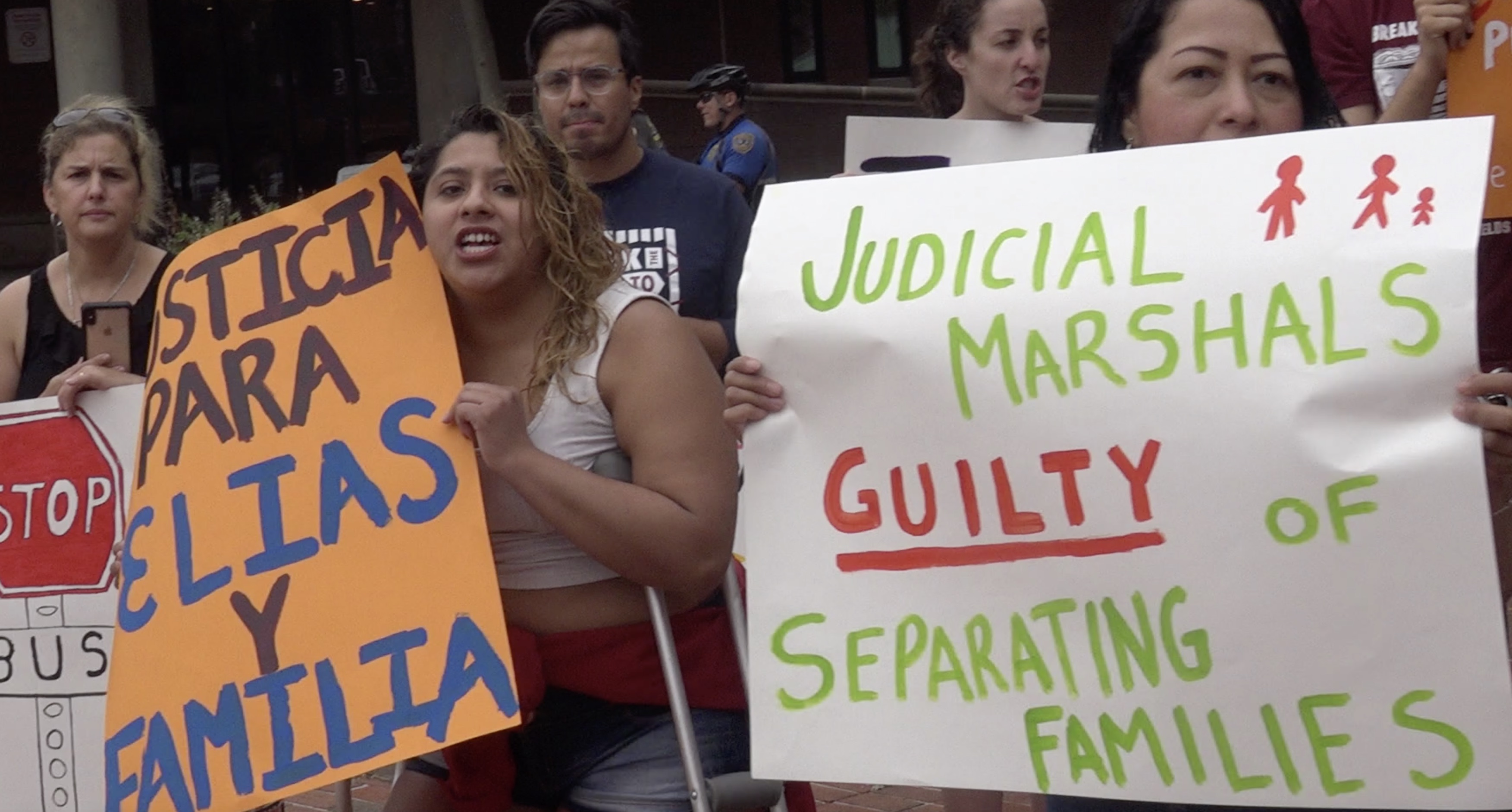 Two activists hold signs. one reads "judicial marshals guilty of separating families"