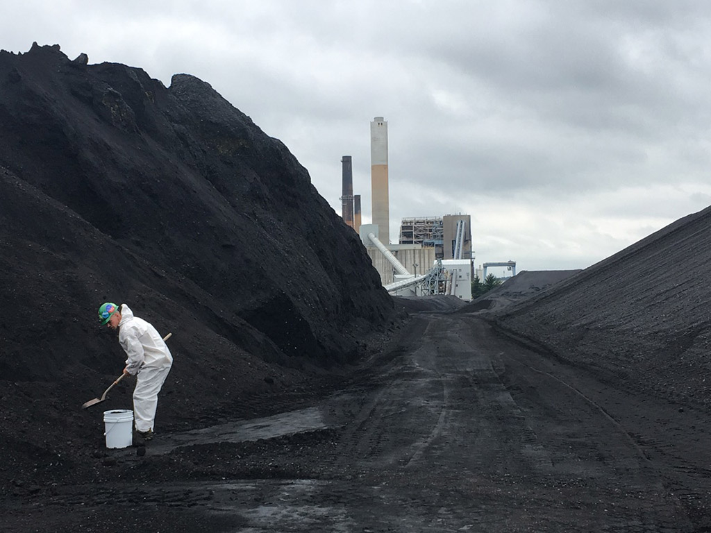 A climate activist wearing white coveralls shovels coal into a bucket at Merrimack Generating Station in Bow, New Hampshire.
