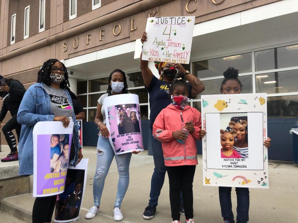Family of Ayesha Johnson gather outside the Suffolk County Jail in Boston, August 4. They stand together and hold hand made signs with pictures of Johnson and slogans for justice.