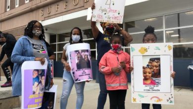 Family of Ayesha Johnson gather outside the Suffolk County Jail in Boston, August 4. They stand together and hold hand made signs with pictures of Johnson and slogans for justice.